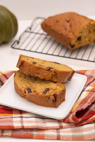 whole loaf chocolate chunk pumpkin bread on cooling rack, slices pumpkin bread on plate