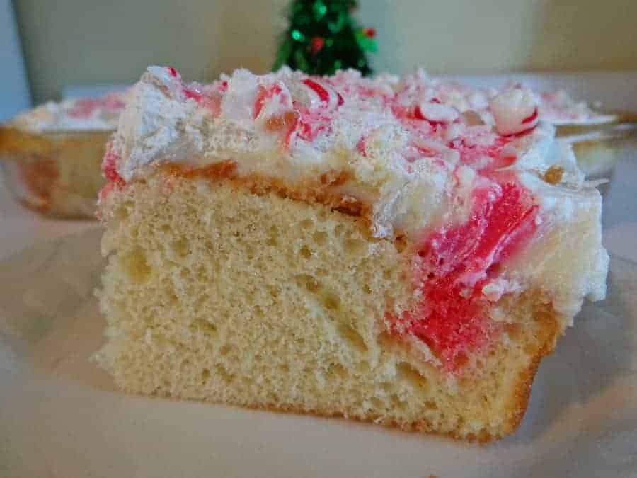 slice of White Chocolate Peppermint Poke Cake on a white plate with whole cake in the background.