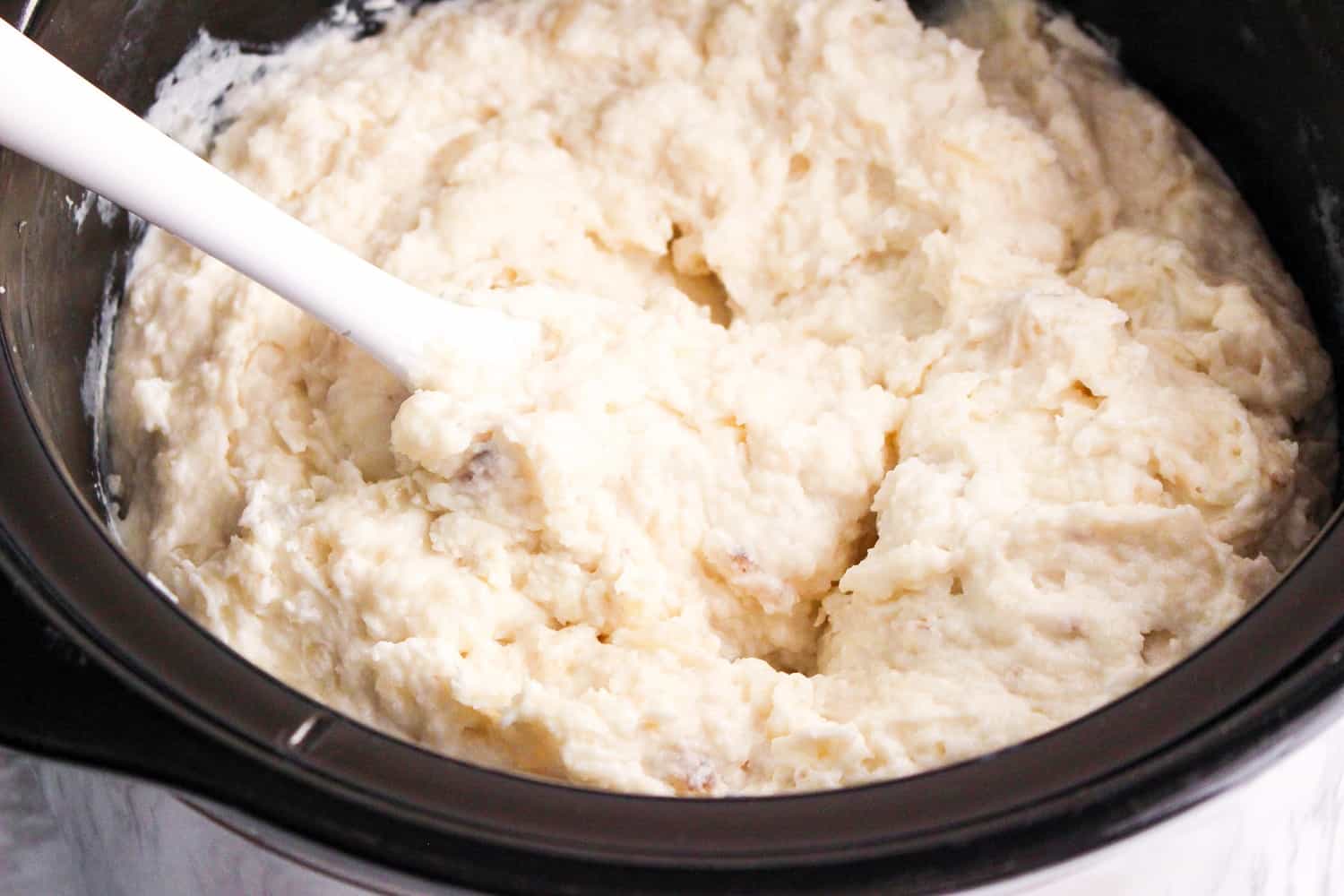 the best slow cooker mashed potaoes recipe in a slow cooker with white spoon