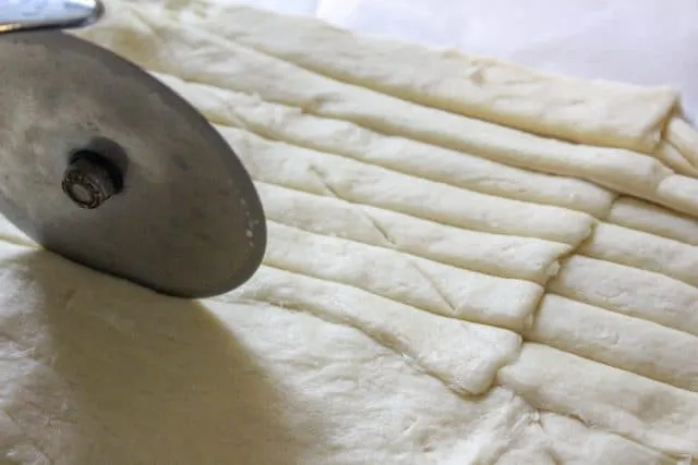 Then using a knife or a pizza cutter, cut the crescent dough into long strips.  