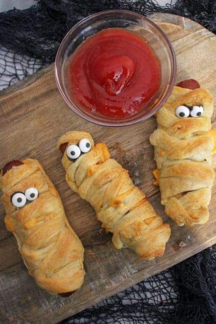 mummy hot dogs on cutting board with ketchup in glass bowl