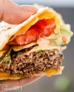 slice of quesadilla burger with lettuce and tomato being held by hand