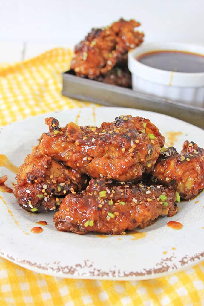 Air Fryer Korean BBQ Chicken Wings on a plate with drizzled sauce, bowl of extra sauce and plate chicken wings