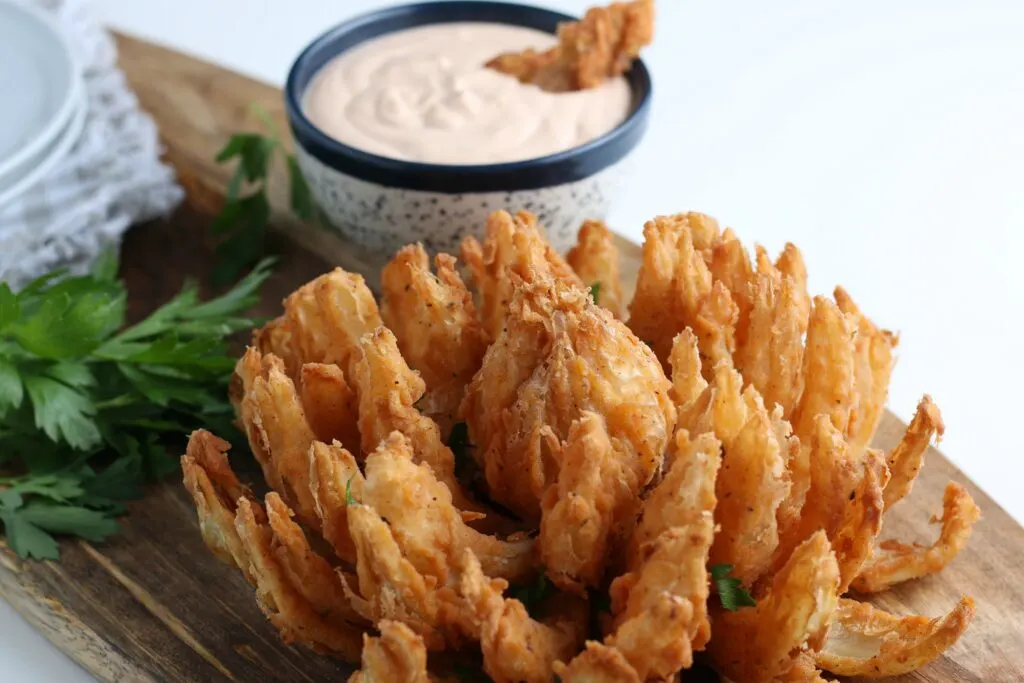 Blooming onion hero shot with dipping sauce and parsley, on a board with dishes