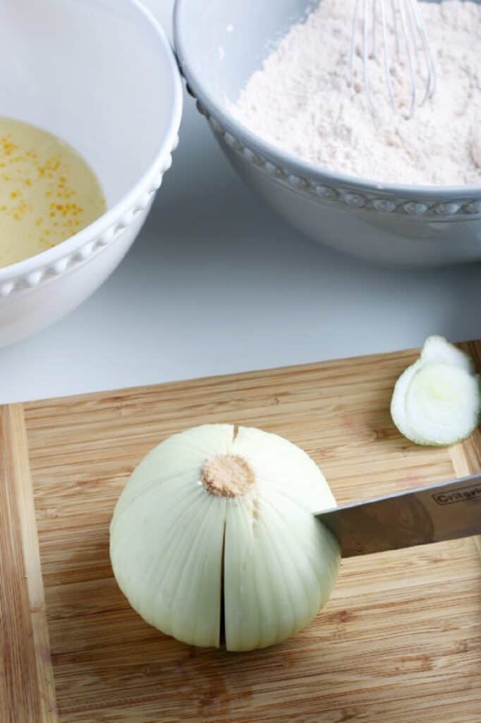 Large white onion prepping for cutting for blooming onion on a board, egg mixture, flour mixture in separate bowls