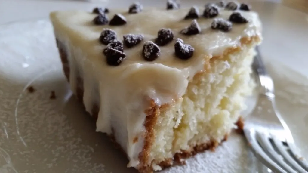 Cannoli Poke Cake made with a white cake mix, slice of cake on white plate with a fork
