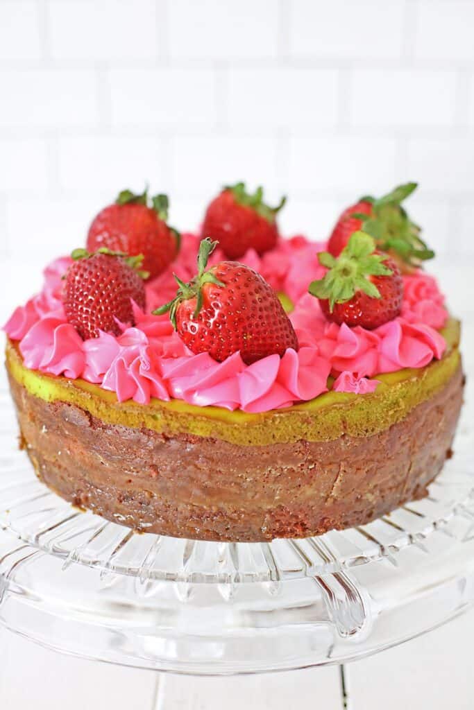 full size key lime strawberry cheesecake cake with pink frosting piped and fresh strawberries