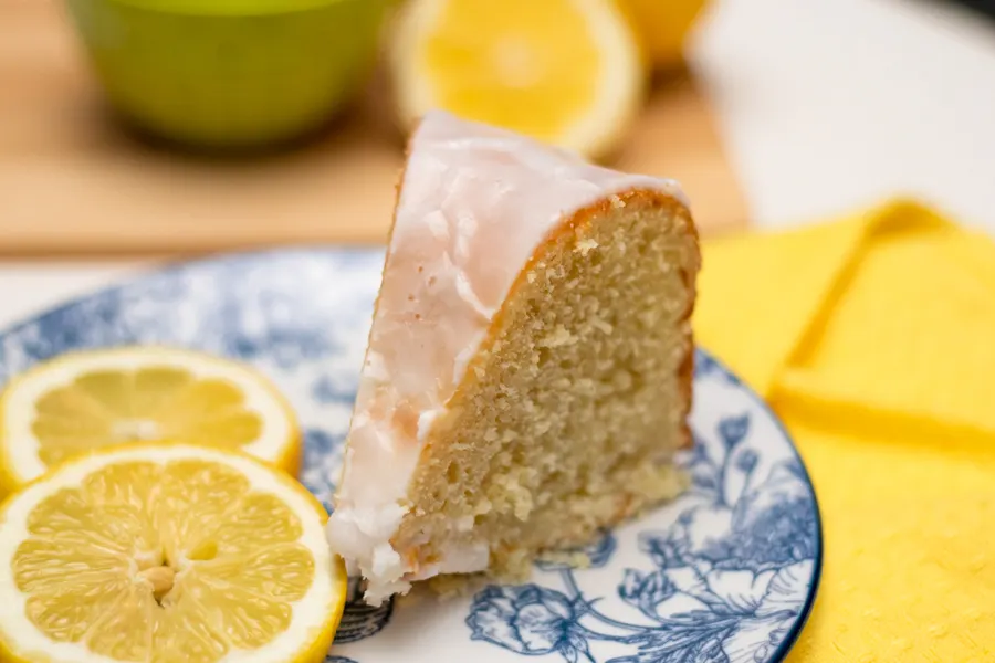 slice of lemon cream cheese bundt cake on blue plate with lemon slices