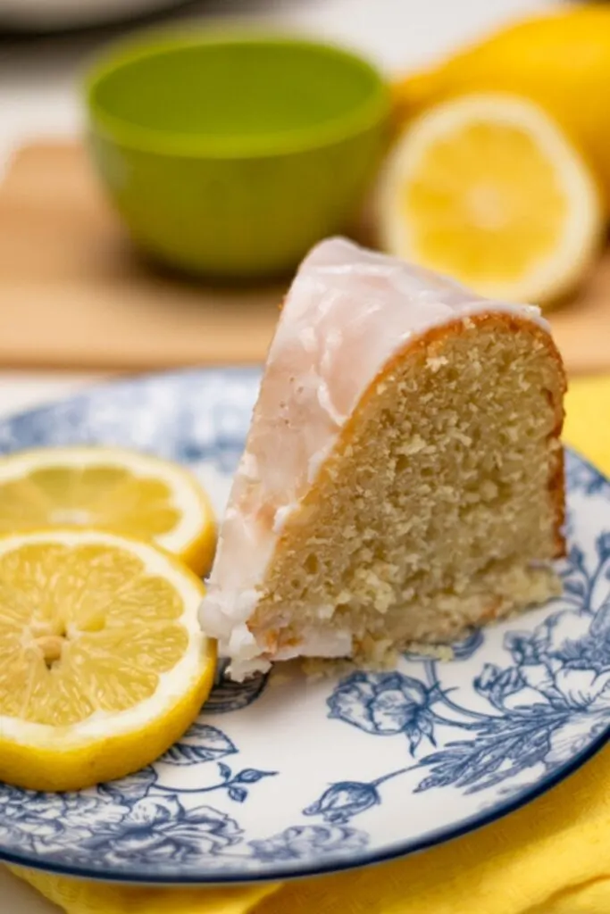Lemon Cream Cheese Bundt Cake with glaze lemon zest over wooden board cake sliced served on blue and white plate