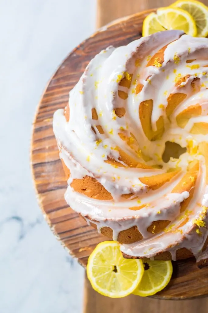 Top view of Lemon Cream Cheese Bundt Cake with glaze and lemon zest over round wooden board and lemon slices