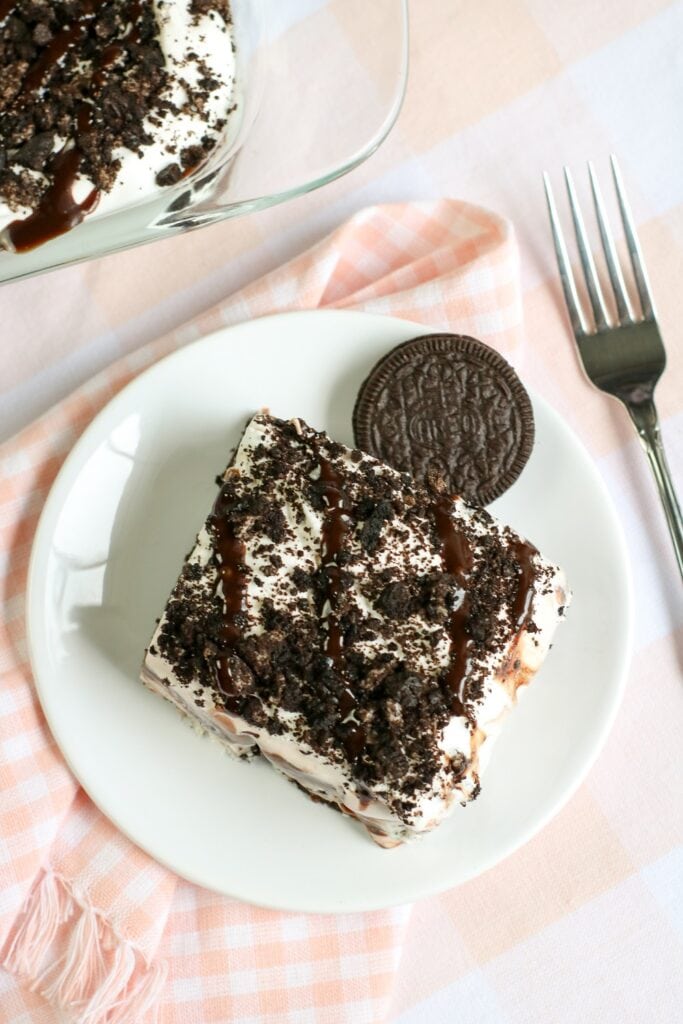 ready to dig in, this no bake oreo cookie delight layered dessert is served on a white plate, pink and white checked napkin and silver fork