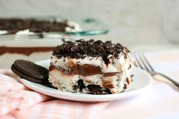 slice of no bake oreo delight on a white plate with the oreo delight in a glass dish