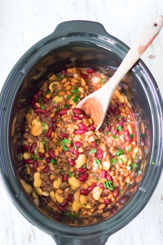 slow cooker beefy baked beans in slow cooker with a wooden spoon