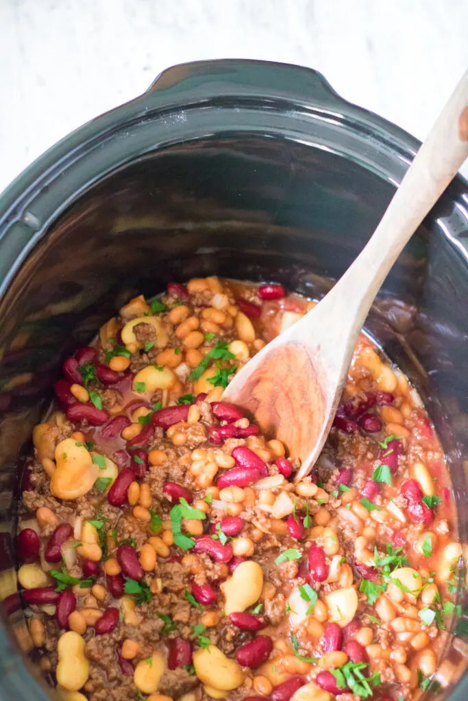 ready to serve to guests, slow cooker beefy baked beans in slow cooker and a wooden spoon to serve.