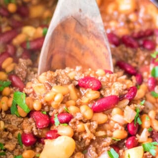 slow cooker beefy baked beans in slow cooker with wooden spoon serving