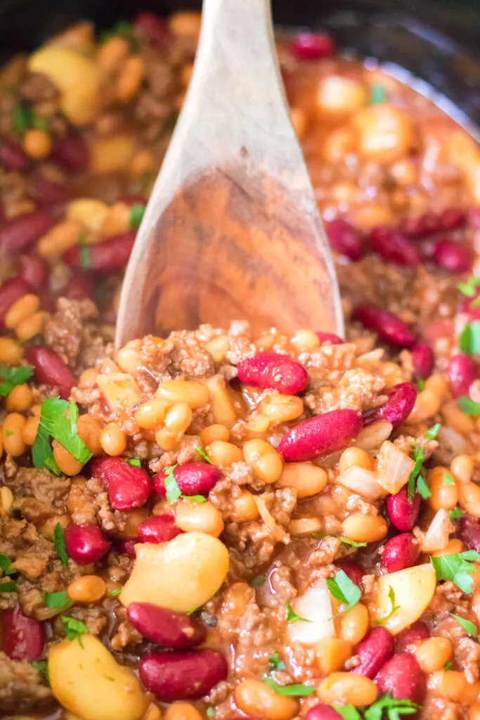 close up of slow cooker beefy baked beans and wooden serving spoon