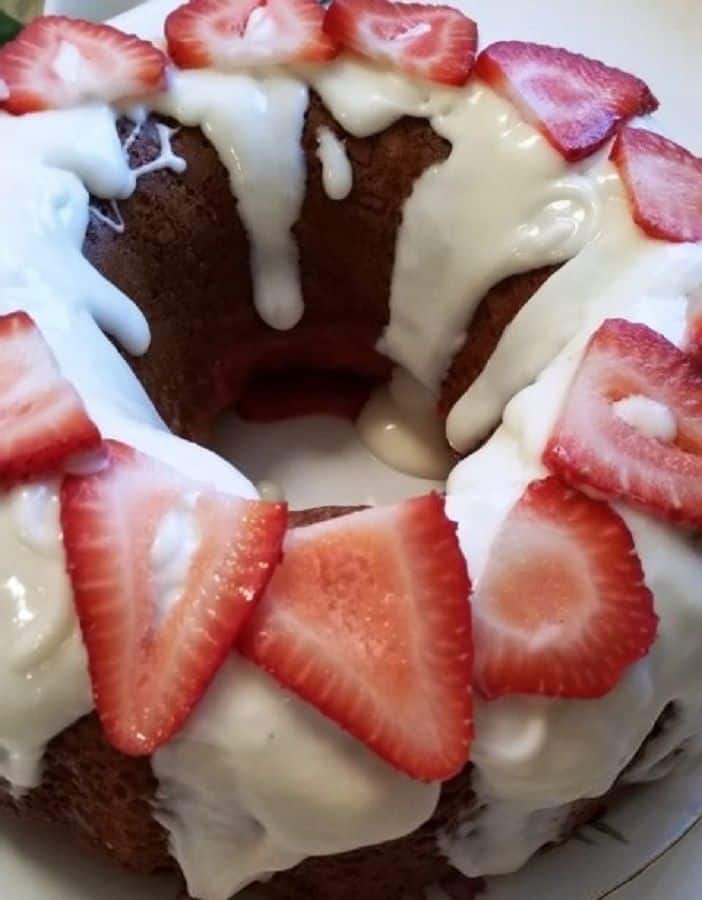 Strawberry Shortcake Poke Cake covered in frosting and sliced strawberries on a platter