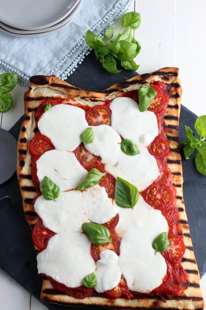 Hero shot grilled Margherita Pizza with fresh basil, tomato sauce, tomatoes, basil, cutting board, plates, napkins