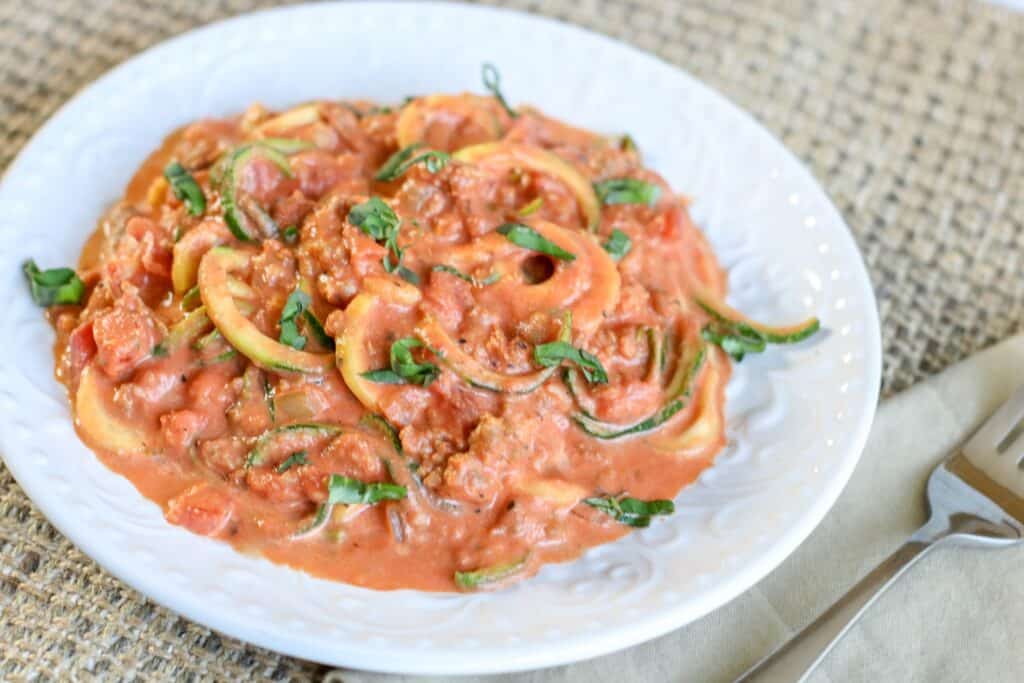 zoodles low carb meal with creamy tomato and sausage sauce in a white bowl fork and napkin
