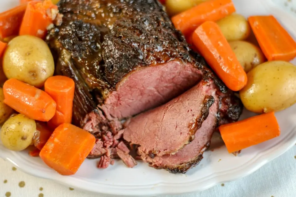 Cooked Corned Beef sliced on platter, potatoes, carrots.
