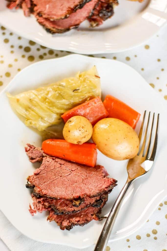 Sliced corned beef and cabbage with carrots and potatoes on white platter