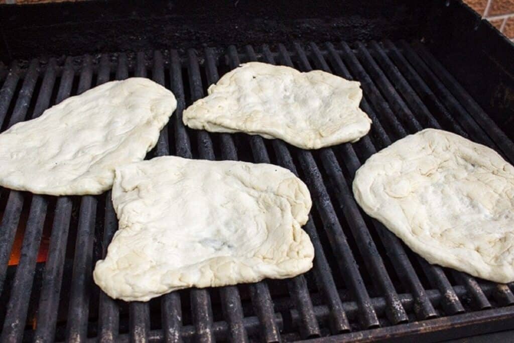 four pieces pizza dough on bbq grill