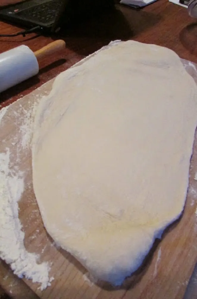 Pizza dough rolled out with a rolling pin on a floured cutting board