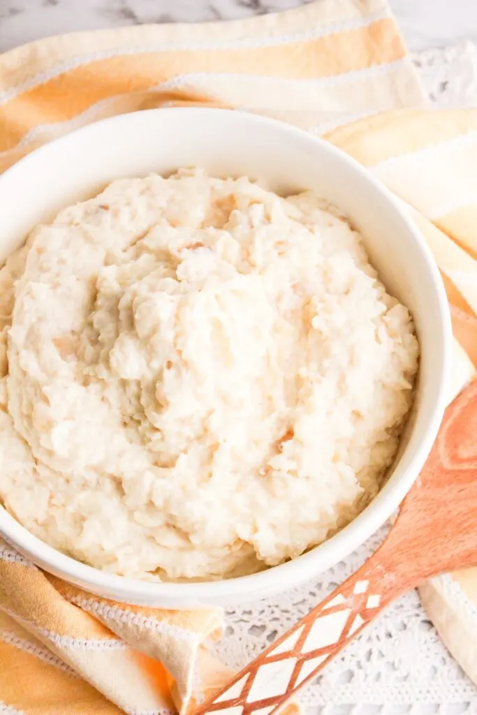 Slow cooker mashed potatoes served in a white bowl with orange and white towel and wooden spoon