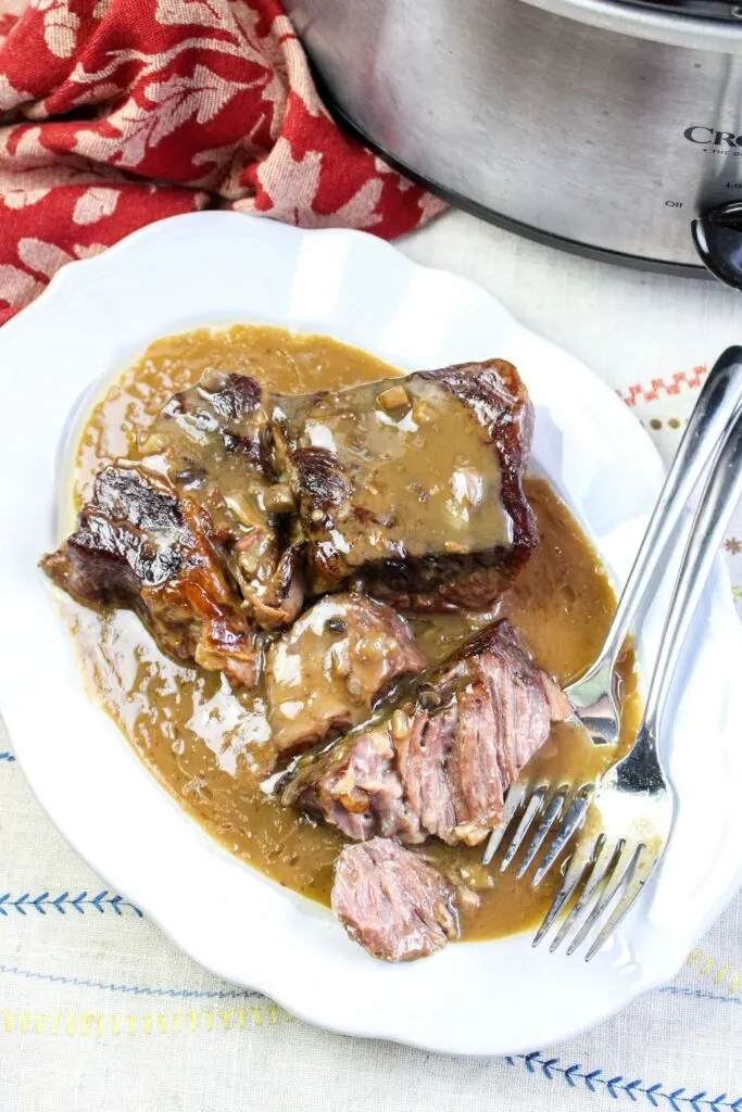 slow cooker roast beef and gravy from above shot vertical served platter with forks crock pot and red towel white tablecloth