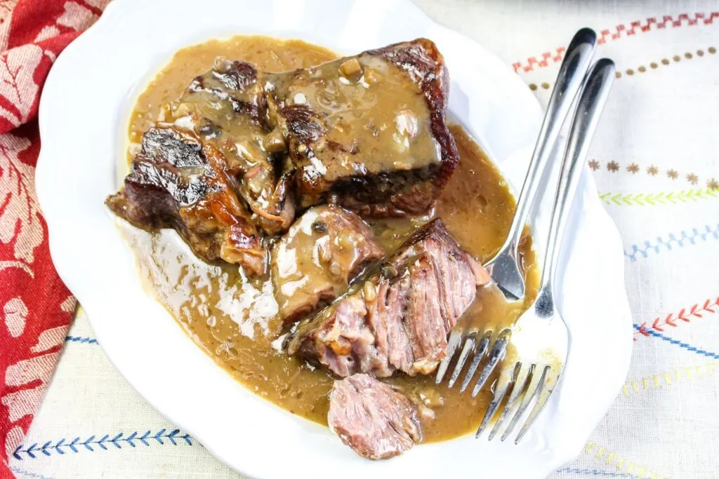 slow cooker roast beef and gravy vertical image served on a white platter with forks shredded beef crock pot and red towel on a white table cloth
