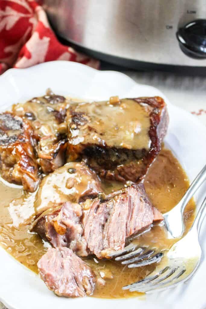 slow cooker roast beef and gravy vertical image served on a platter with forks crock pot and red towel
