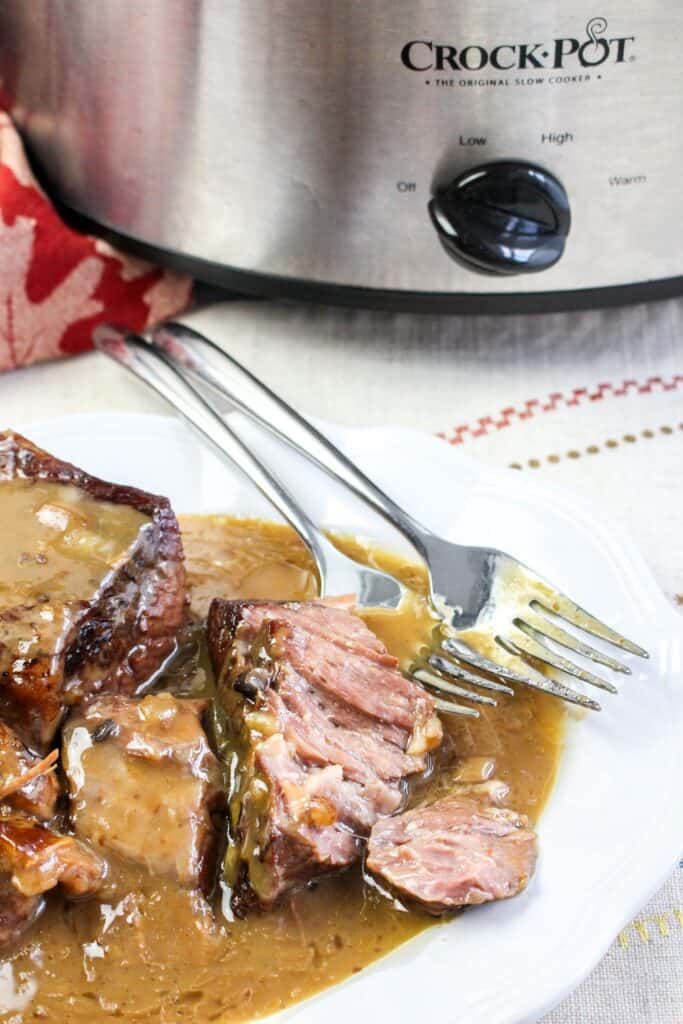 slow cooker roast beef and gravy close up of shredded beef shot vertical served platter with forks crock pot and red towel on a white tablecloth