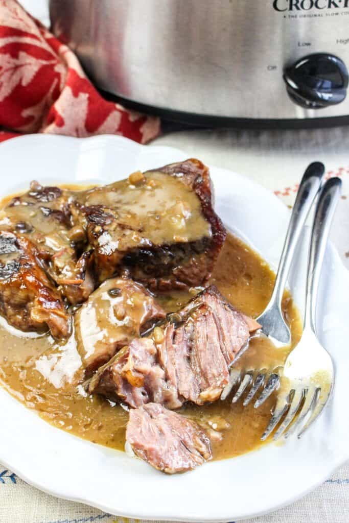 slow cooker roast beef and gravy hero shot vertical served platter with forks crock pot and red towel