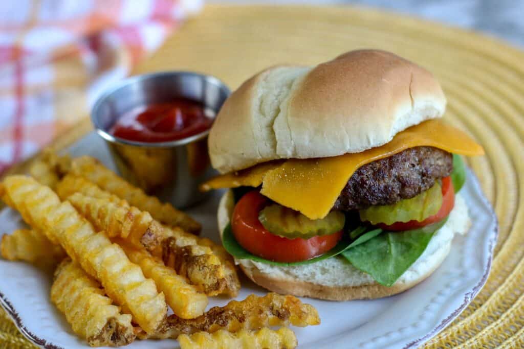 vertical shot air fryer burger with cheese pickles tomato lettuce on a bun french fries and ketchup on plate over placemat with checked towels