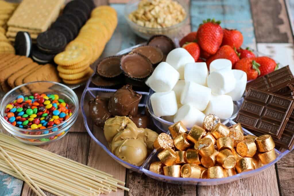horizontal crackers, cookies, berries, peanut butter cups, marshmallows, m and m's peanut butter nutella all of the ingredients for S'mores Board laid out
