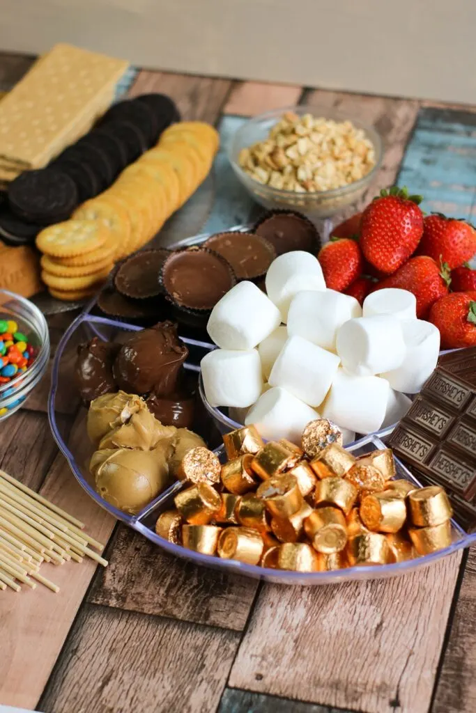crackers, cookies, berries, peanut butter cups, marshmallows, m and m's all of the ingredients for S'mores Board laid out vertical
