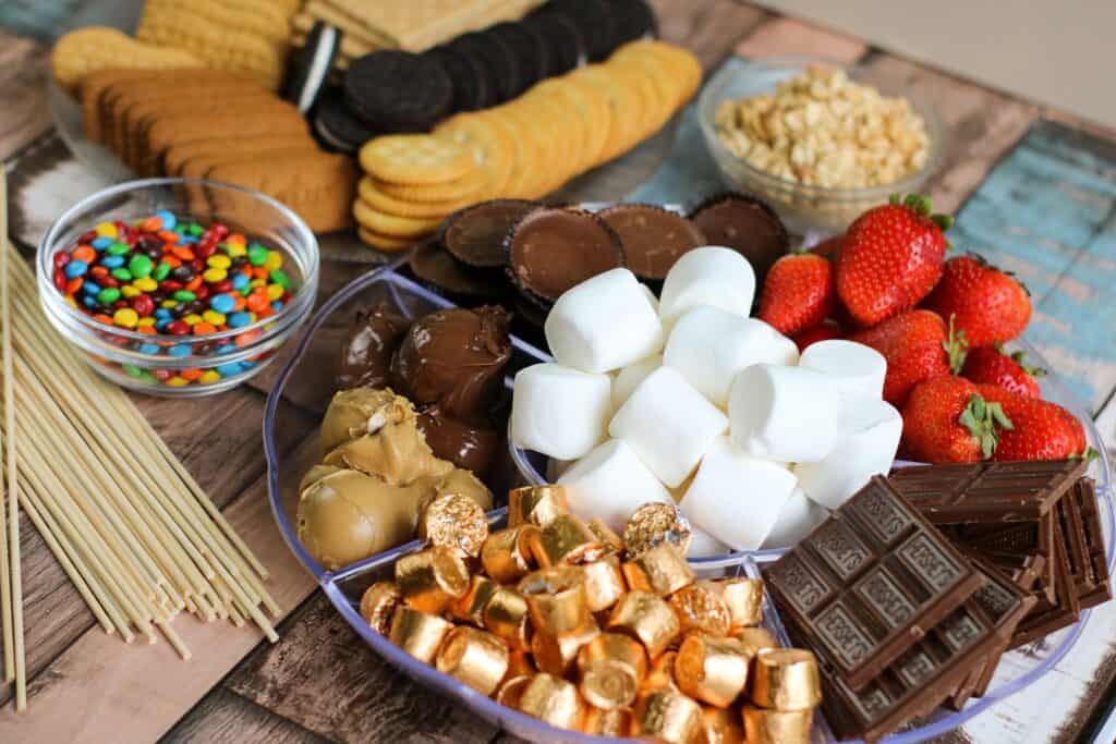horizontal crackers, cookies, chocolate bars, berries, peanut butter cups, marshmallows, m and m's all of the ingredients for S'mores Board laid out 