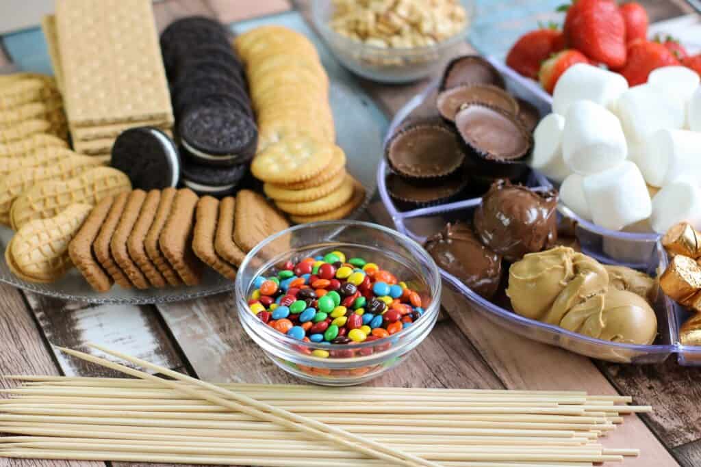 horizontal crackers, cookies, berries, peanut butter cups, marshmallows, m and m's all of the ingredients for S'mores Board laid out