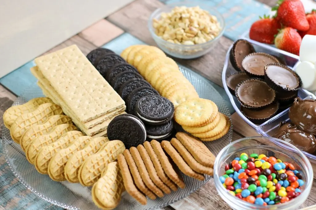 crackers, cookies, berries, peanut butter cups, marshmallows, m and m's all of the ingredients for S'mores Board laid out horizontal