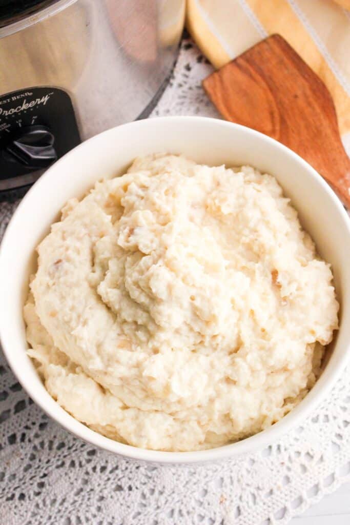 Slow Cooker Mashed Potatoes in a white bowl with slow cooker background over lace tablecloth