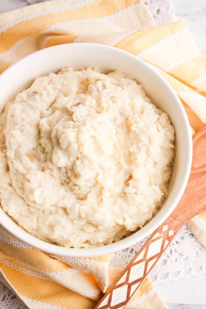 slow cooker mashed potatoes served in a white bowl over orange and white towel and wooden spoon
