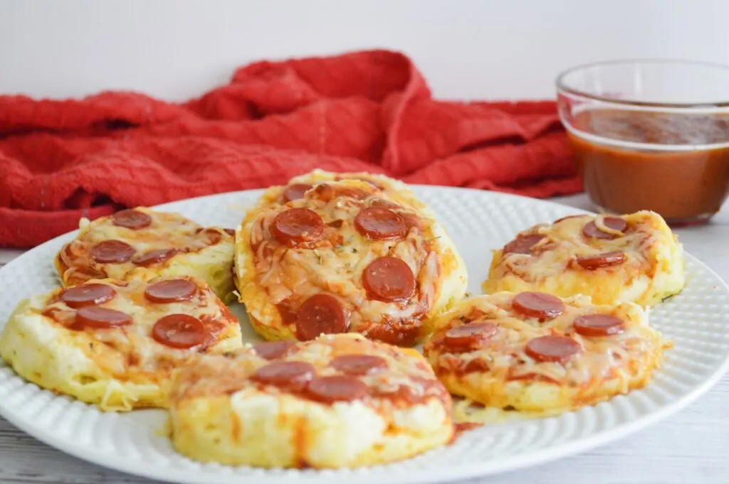 mini pepperoni pizzas on white serving plate marinara sauce in clear bowl red towel