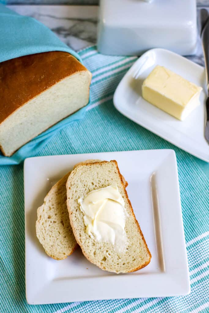 Bread in a bag hero vertical shot loaf cut served with pat of butter butter dish on blue tablecloth