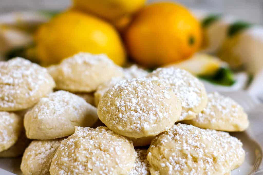 Horizontal shot  Lemon Cookies on a platter with lemons in a green and white bowl
