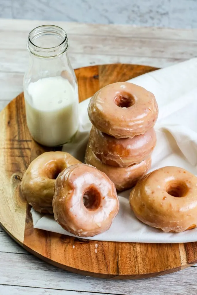 Homemade yeast doughnuts with a vanilla glaze stacked doughnuts with milk jug on wooden board and white napkin