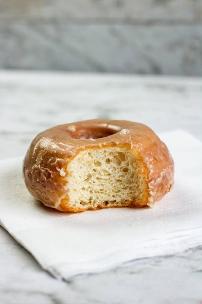Homemade yeast doughnut with a vanilla glaze bite taken out white napkin