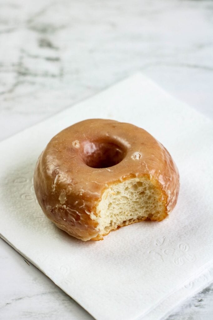 Homemade yeast doughnuts with a vanilla glaze with bite taken out of doughnut on napkin 