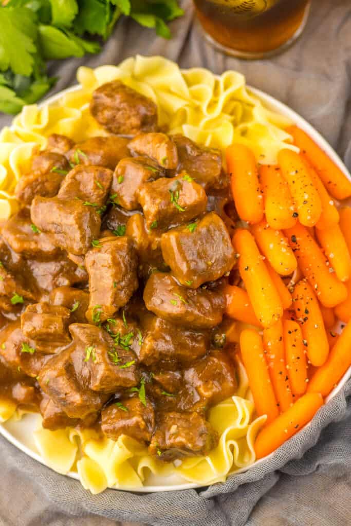 beef tips, noodles, carrots in bowl with gray background