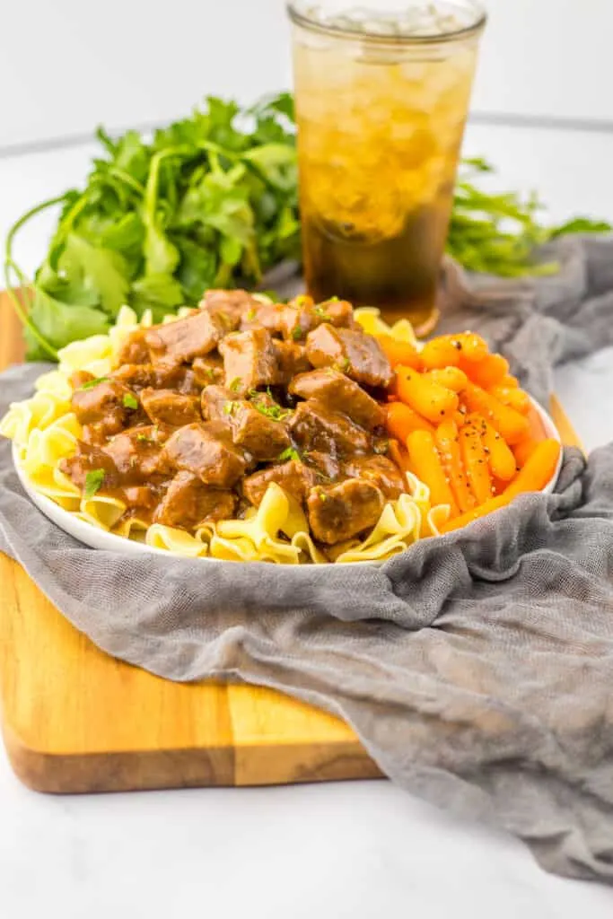 beef tips and gravy over noodles in bowl gray napkin wood board lettuce glass tea