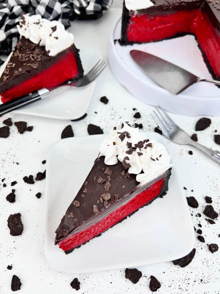 slice of red velvet cheesecake on white plate with cookie crumbs